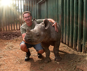 zookeeper assistant squatting next to a baby rhinoceros
