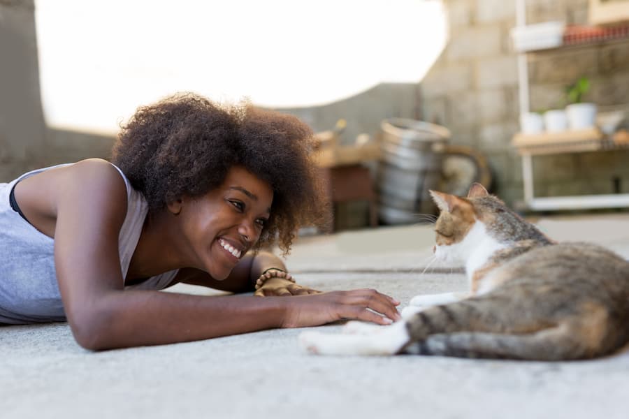 Smiling black woman lies on floor with an attentive cat in training