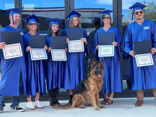 Six ABC dog obedience training graduates pose with a sitting German shepherd 