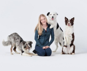 Service dog training expert Sara Carson kneels on the floor surrounded by three large dogs