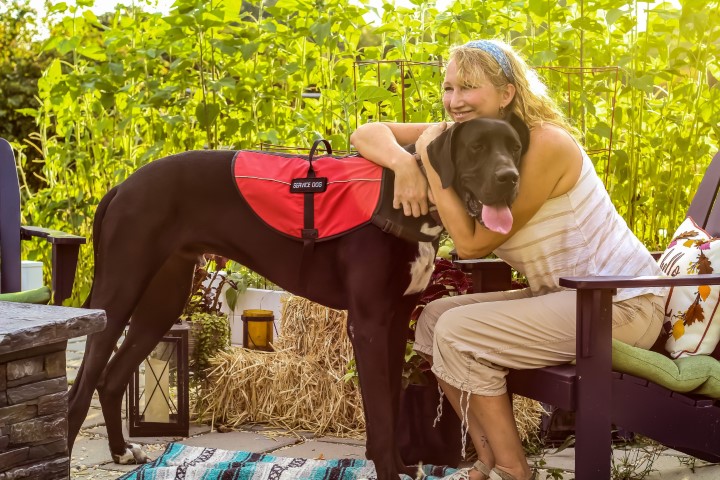 Older woman on patio hugging her large black service dog