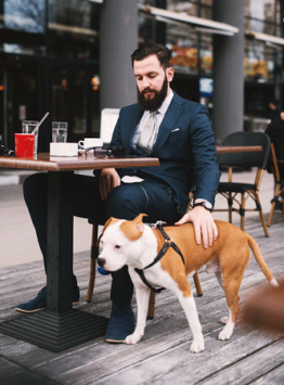 businessman-at-coffee-shop-with-dog Man sitting at a small cafe table pats his trained service dog