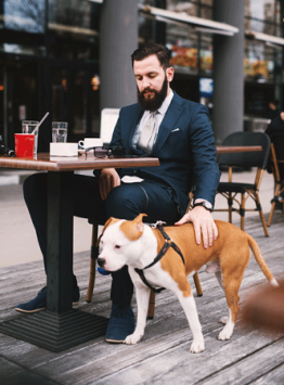 Man sitting at a small cafe table pats his trained service dog